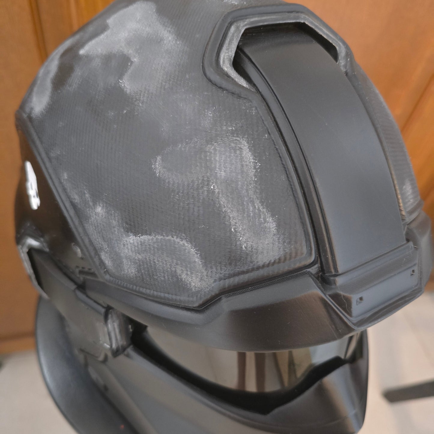 A black welding helmet with a textured front shield, photographed from an overhead angle on a wooden floor.