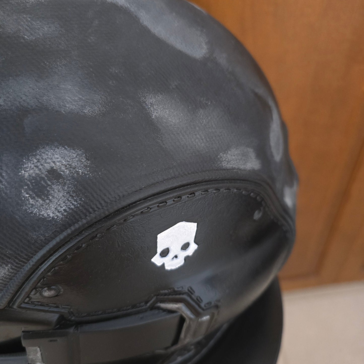Close-up of a black motorcycle helmet with a white skull logo on the side, resting on a wooden surface.