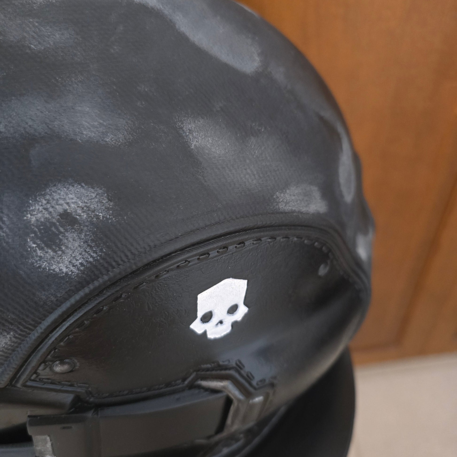 Close-up of a black motorcycle helmet with a white skull logo on the side, resting on a wooden surface.